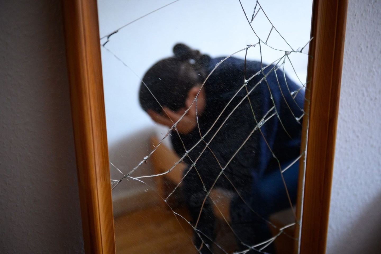 Eine Frau sitzt neben einem gesprungenen Spiegel auf einem Bett und hält ihren Kopf in den Händen. (Symbolbild)