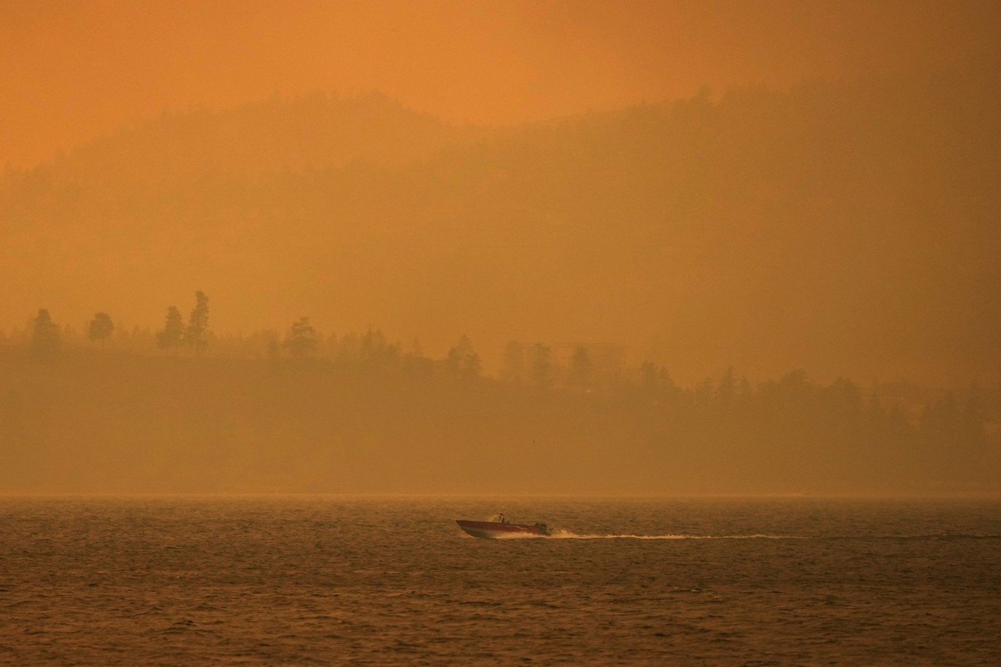 Ein Boot fährt auf dem Okanagan-See, während der Rauch des McDougall-Creek-Wildfeuers über dem Gebiet liegt.