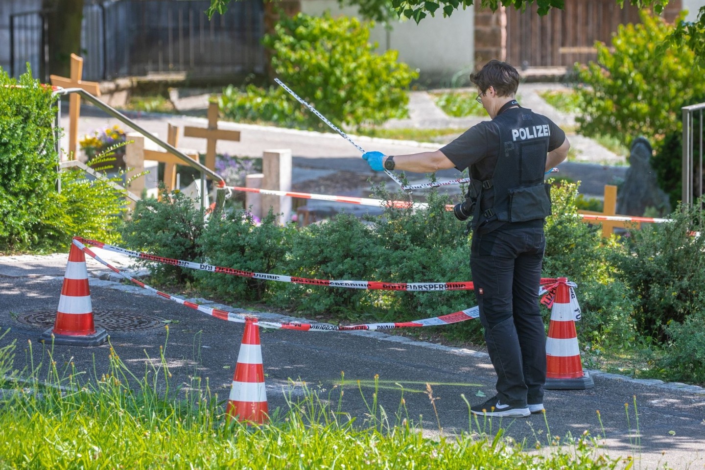 Eine Mitarbeiterin der Spurensicherung vermisst Spuren am Tatort auf einem Friedhof.