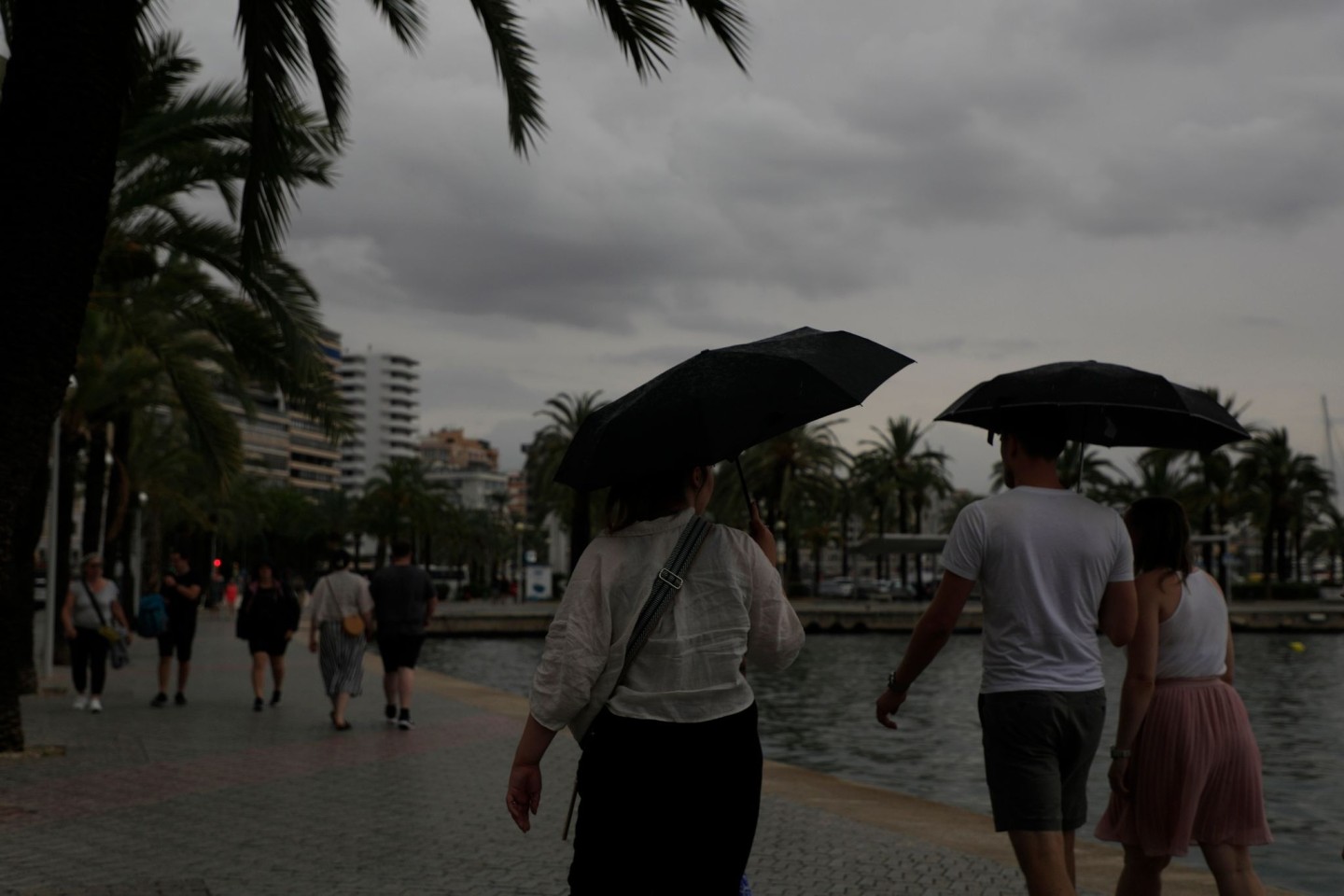 Spaziergänger mit Regenschirmen sind an der Strandpromenade von Palma unterwegs.